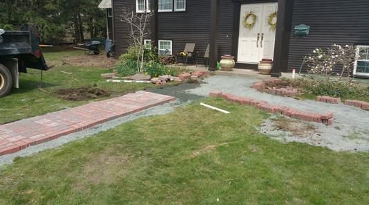 A yard with grass and brick path leading to the house.