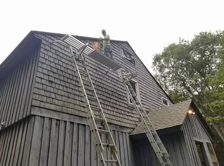 A man on a ladder is climbing up the side of a house.