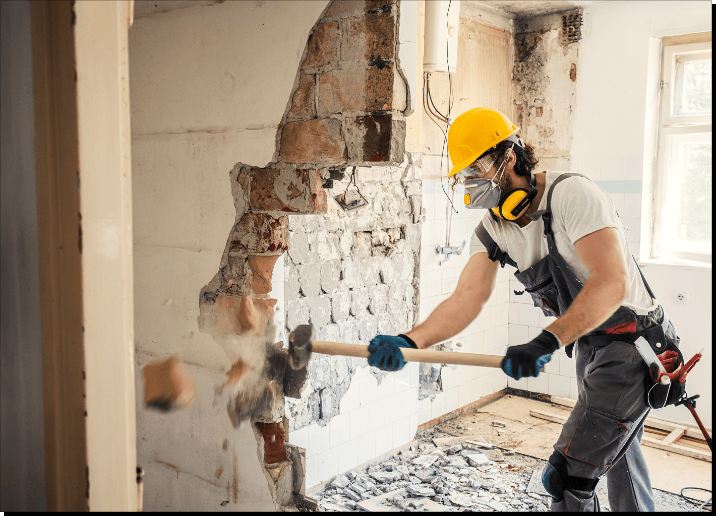 Worker demolishing wall with sledgehammer.